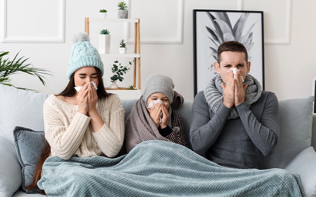 Familie mit Erkältung sitzen auf dem Sofa und teilen sich eine Decke
